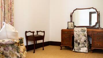 A bedroom with a wooden dresser, a chair, a bed with a floral bedspread, and a large mirror.