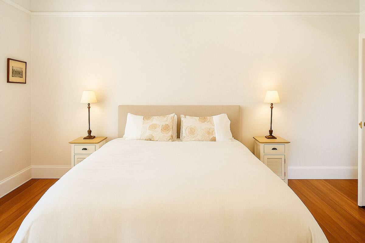 A neatly made bed with a headboard, two bedside tables with lamps, and a framed picture on the wall.