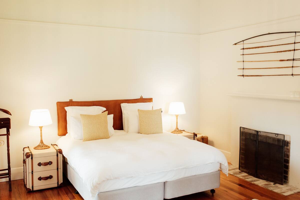 A neatly arranged bedroom with a large bed, bedside tables, lamps, and a fireplace.