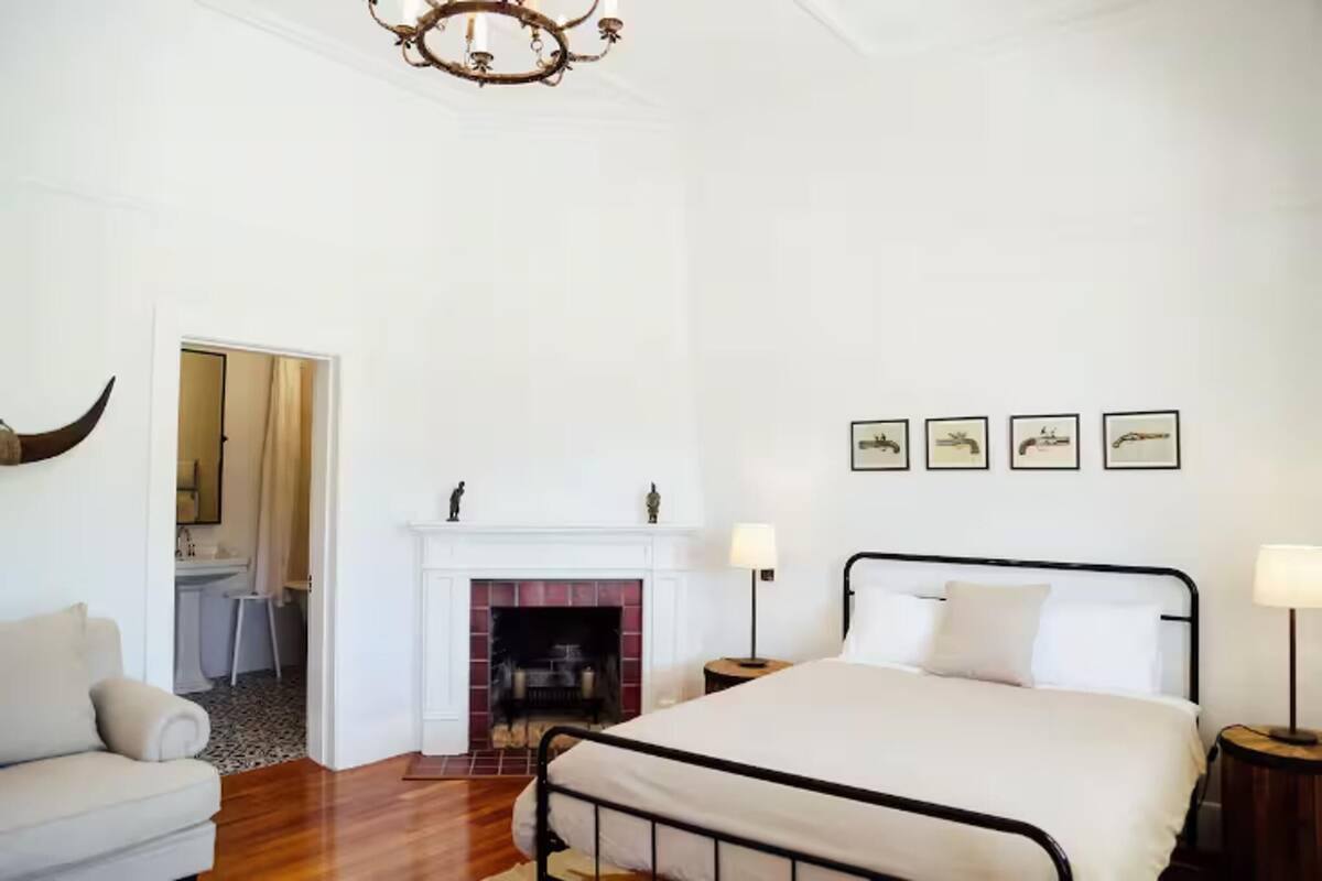 A bedroom with a bed, a fireplace, a chandelier, and framed pictures on the wall.
