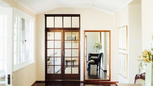 A spacious room with a wooden floor, a large wooden door, and a view into another room with a chair and a table. - Mount William Station (Willaura)