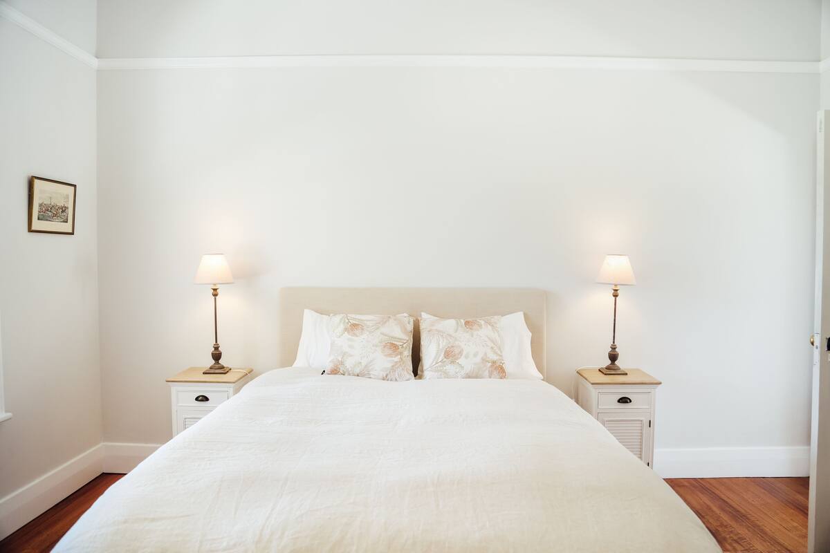 A neatly made bed with a white duvet, two bedside tables with lamps, and a framed picture on the wall.