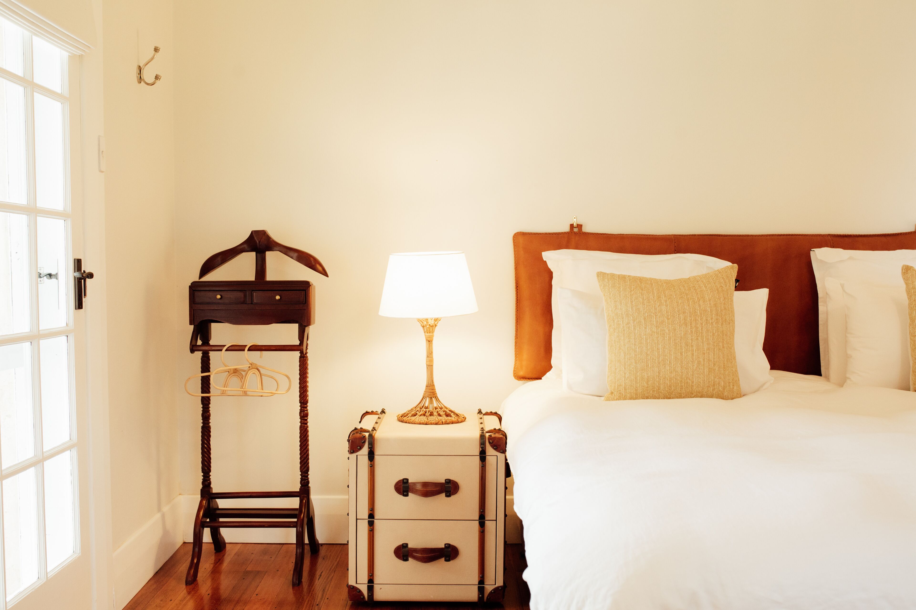 Une chambre d’hôtel avec un lit, une table de chevet avec une lampe, une chaise en bois et une valise.
