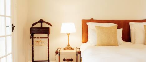 Une chambre d’hôtel avec un lit, une table de chevet avec une lampe, une chaise en bois et une valise.