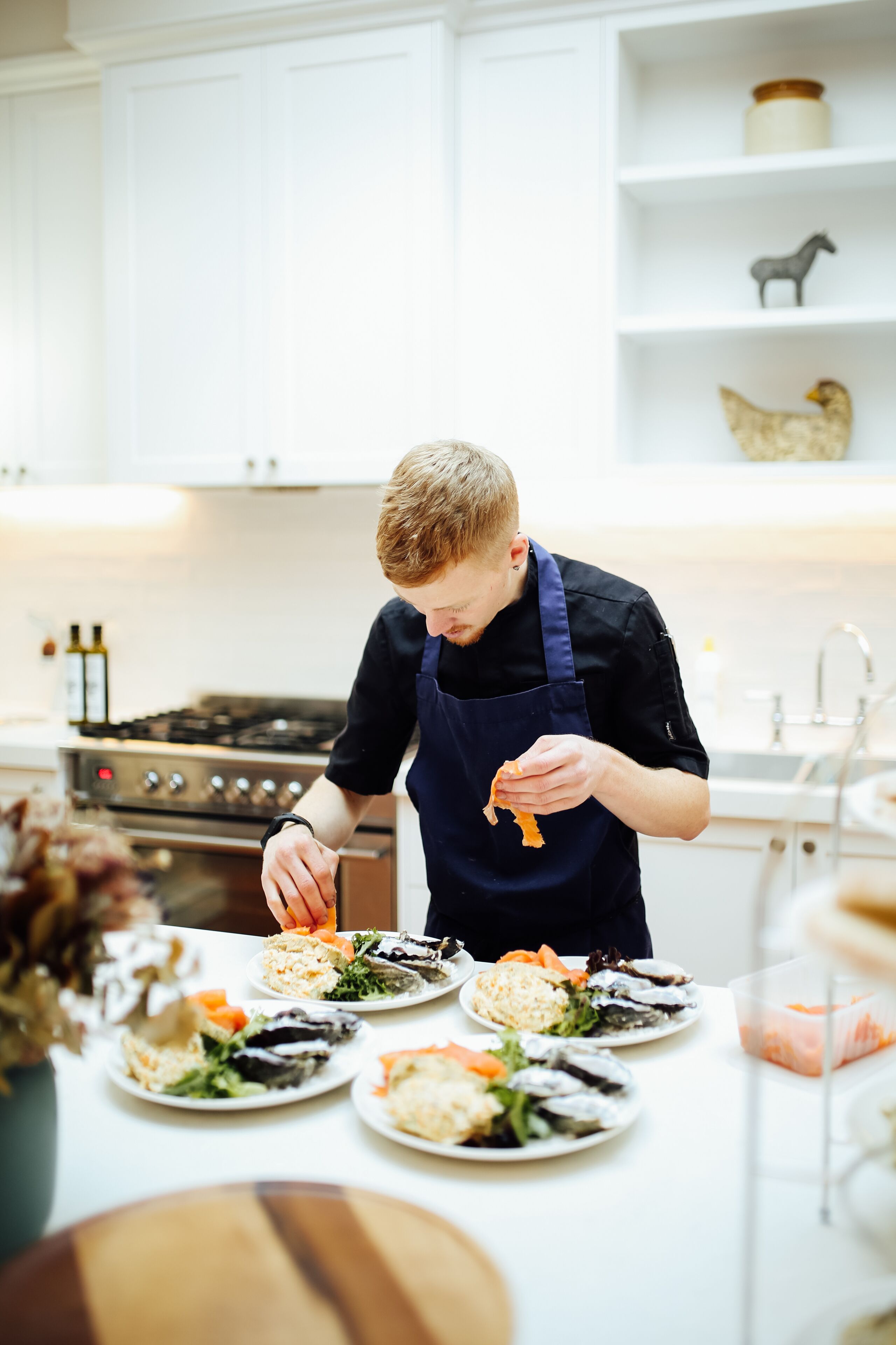 En person laver mad i et køkken med hvide skabe og en komfur.