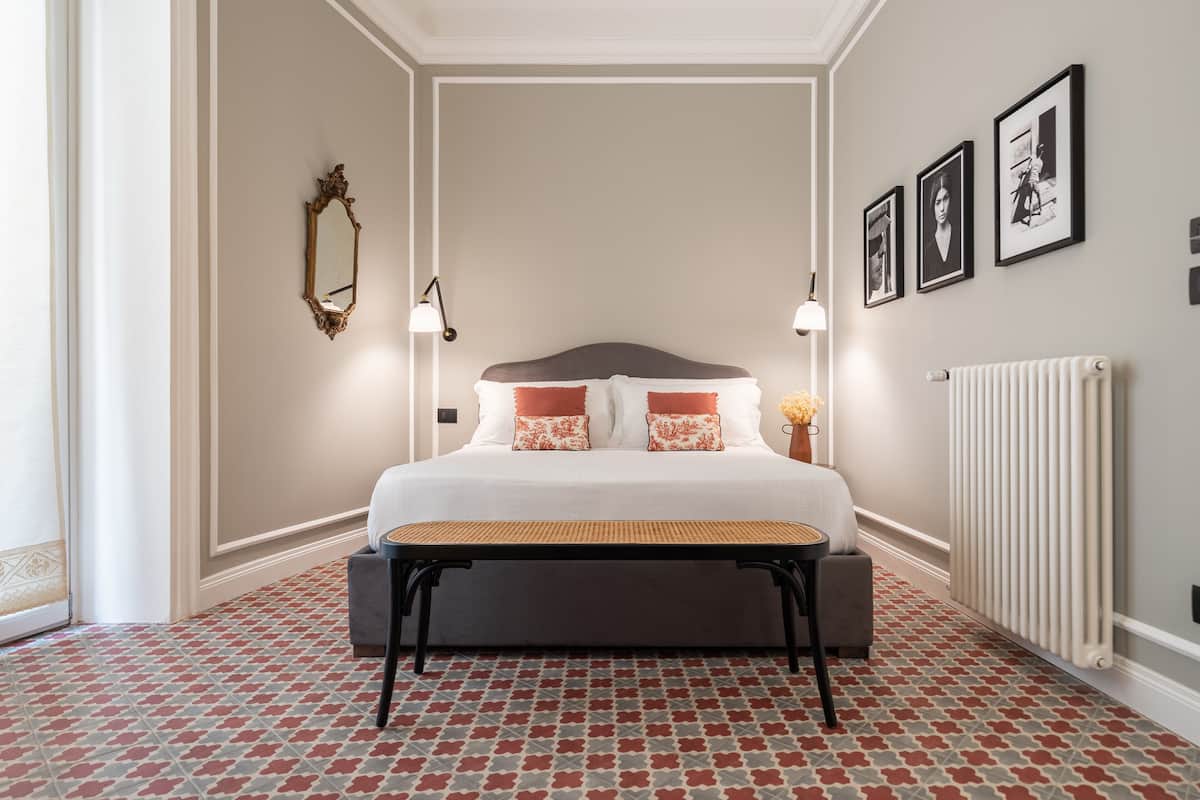 Un dormitorio ordenado con cama, lámparas de noche, un banco y un radiador.