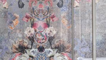 Una stanza con un letto, un muro decorato con un affresco floreale e con uccelli, e un lampadario.
