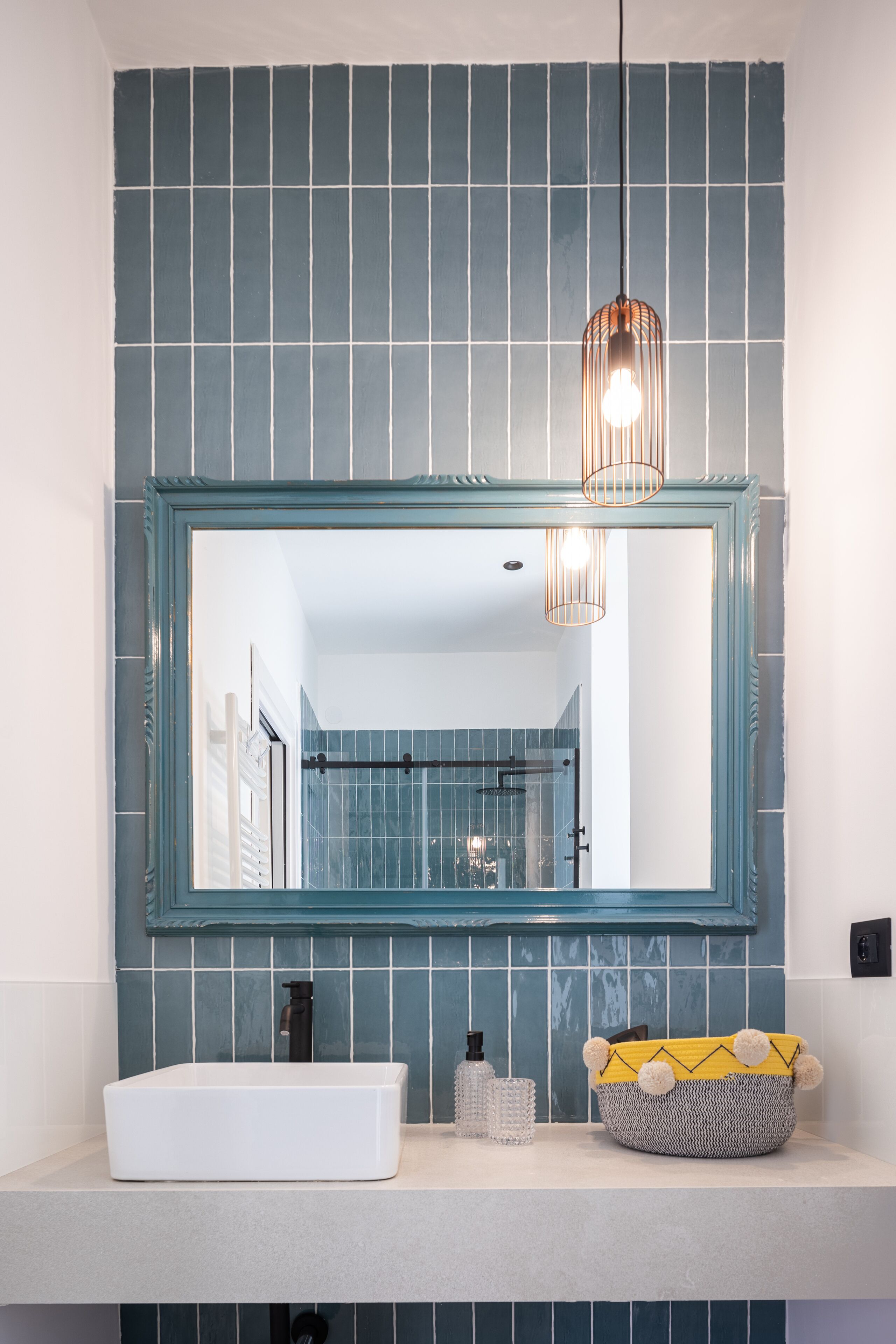 A bathroom with a large mirror, a white sink, a towel rack, and a blue-tiled wall.