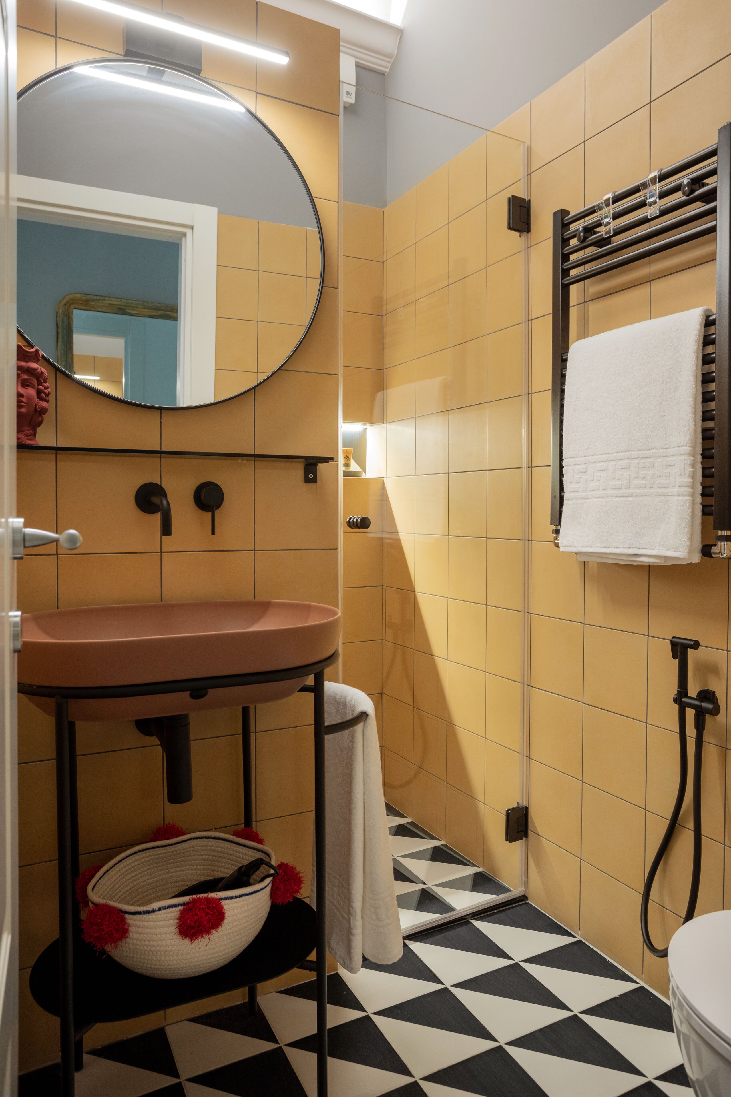 Un baño con un espejo redondo, un lavamanos, un perchero para toallas y un inodoro.