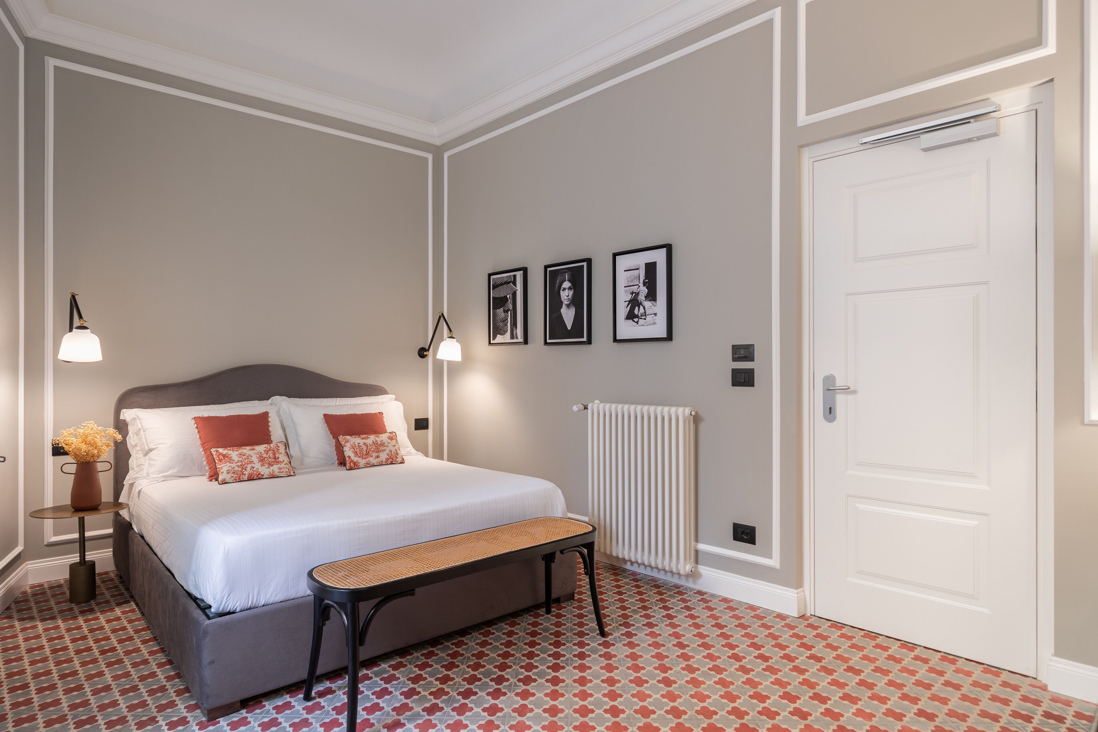 Una camera da letto con un letto, comodini, una panca, un termosifone e quadri appesi al muro.