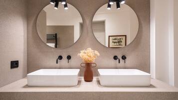 A bathroom with two white sinks, a brown vase with flowers, and two round mirrors with lights.