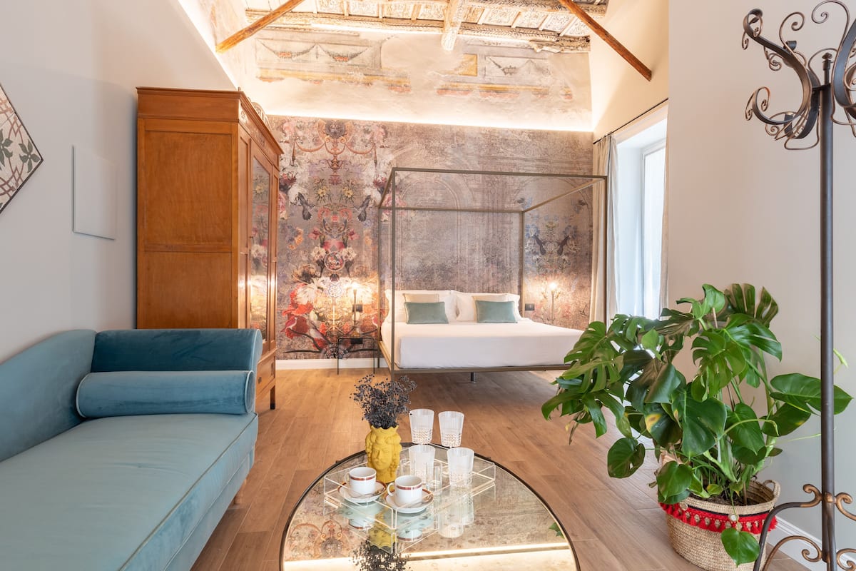 Una habitación moderna con sofá, una mesita de centro de vidrio, cama y una planta grande.