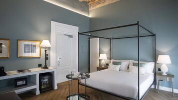 Una habitación de hotel moderna con una cama con dosel, un escritorio con ordenador, un refrigerador pequeño y una mesita de noche con lámpara.