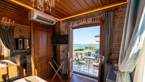 Une pièce dotée d’un plafond en bois, d’un appareil de climatisation, d’un lustre, d’une porte en bois, d’une petite table avec des chaises et offrant une vue sur un balcon aménagé avec du mobilier d’extérieur.
