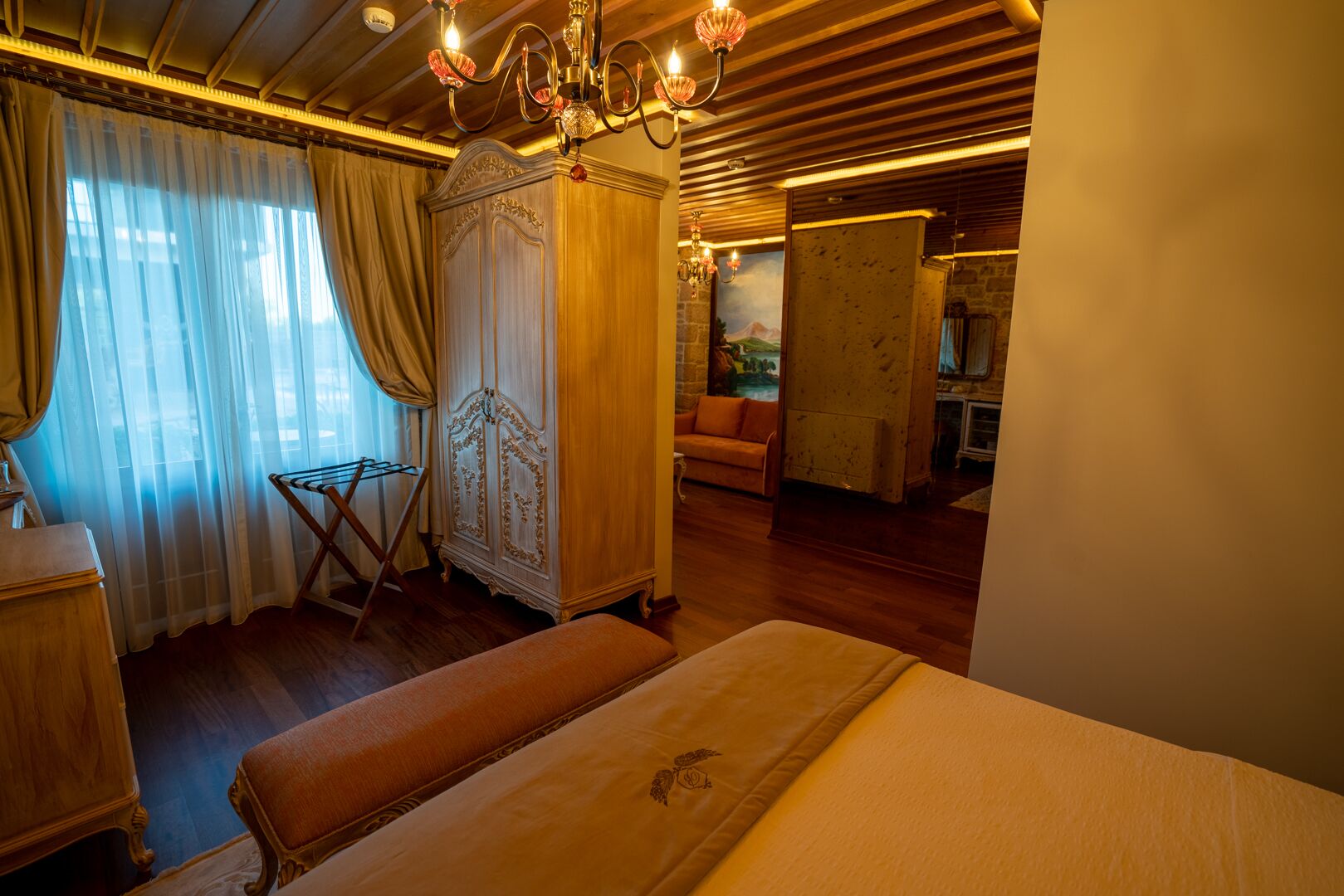 A room with a bed, a wardrobe, a sofa, and a chandelier.