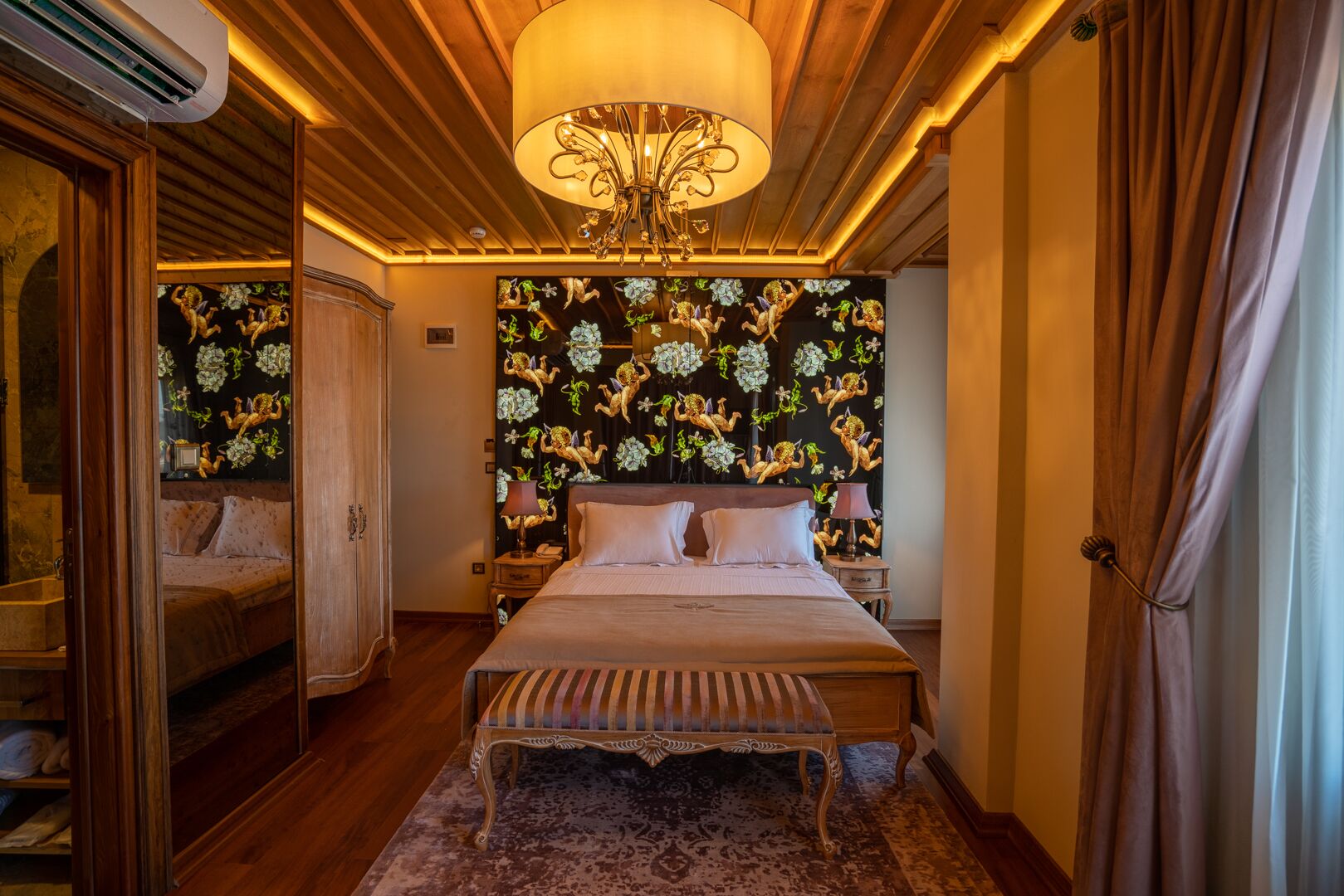 Un dormitorio con una cama grande, una araña, un tocador con espejo y un papel tapiz floral.