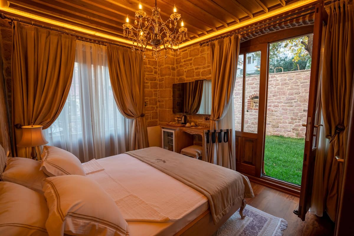 A bedroom with a large bed, a desk, and a view of a garden.