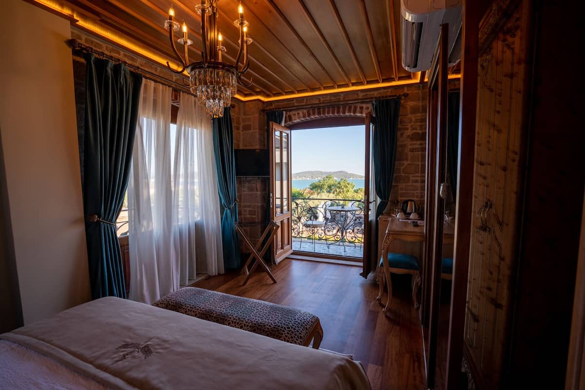 A room with two beds, a chandelier, a balcony with a table and chairs, and a view of the sea.