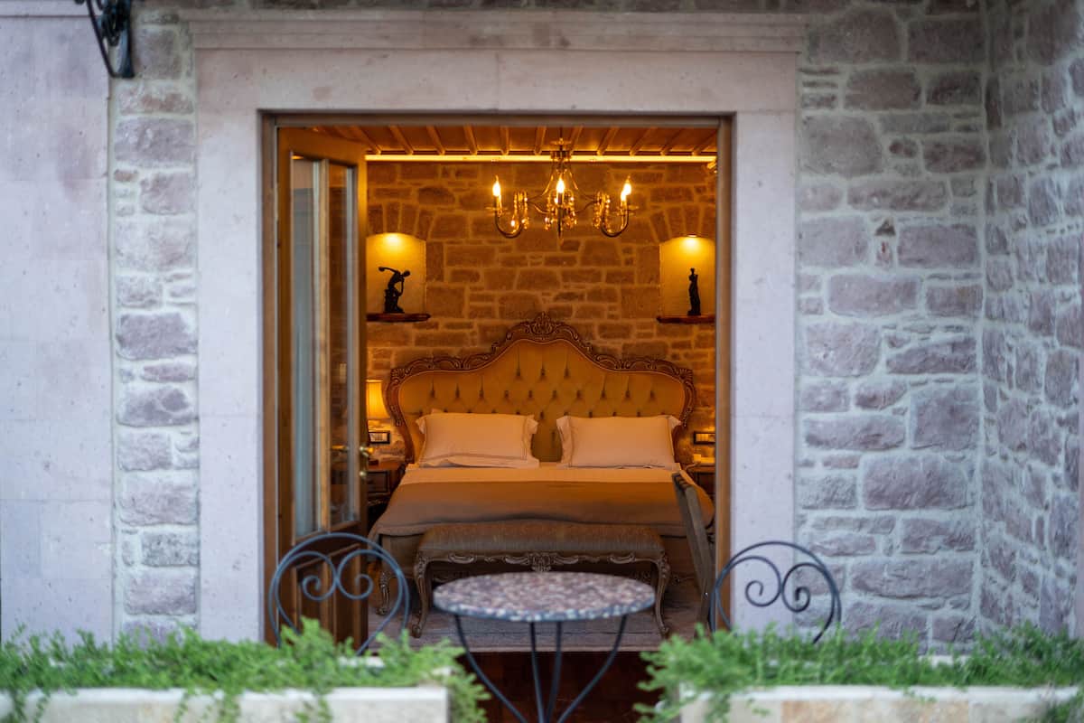 A bedroom with a stone wall, a large bed, two bedside lamps, and a chandelier.