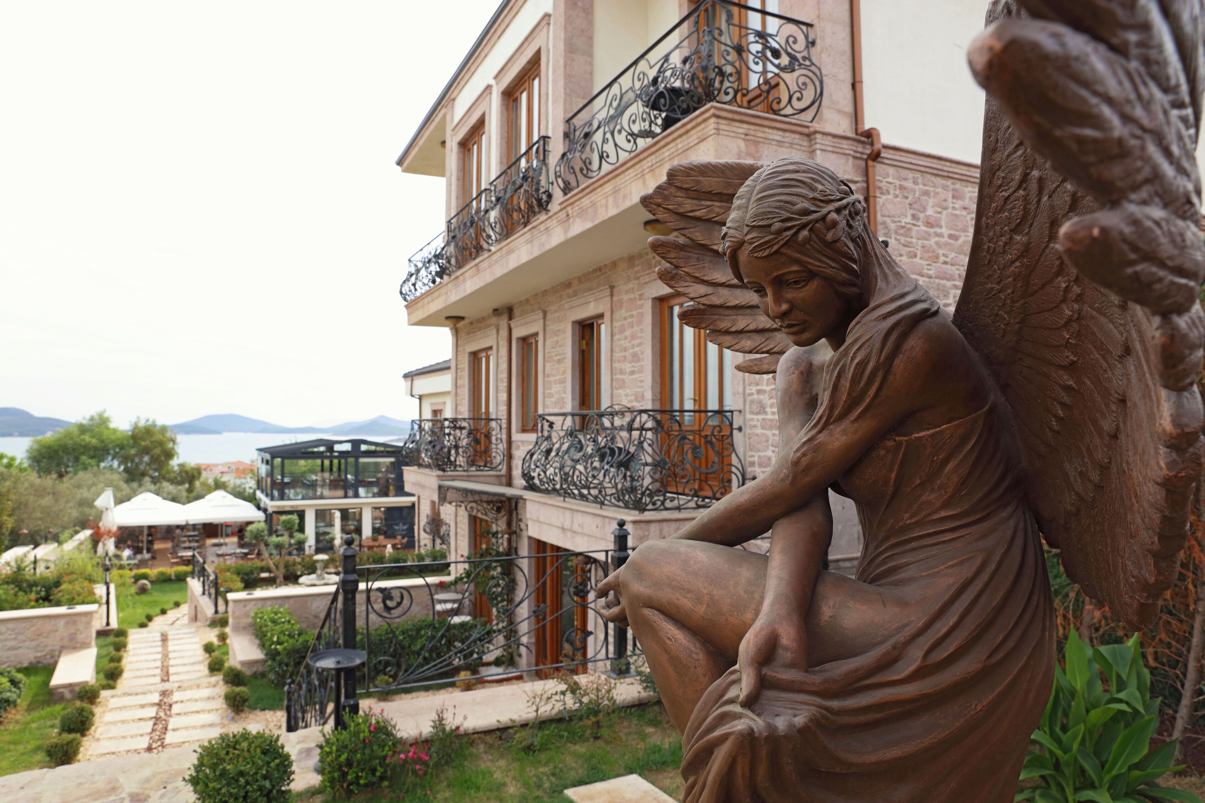 A statue of an angel in a garden setting with a building in the background.