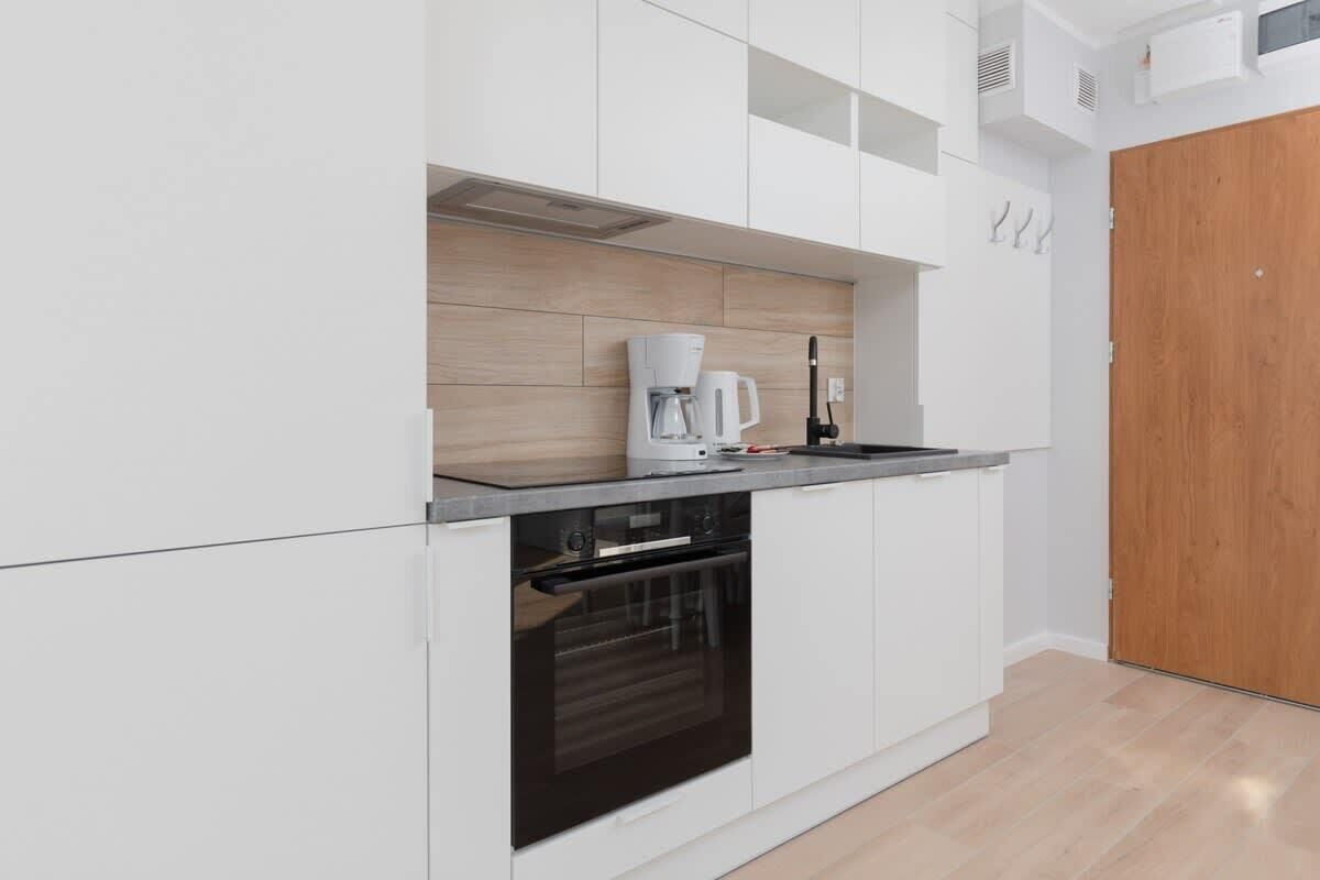 Eine moderne Küche mit weißen Schränken, einem eingebauten Backofen, einer Kaffeemaschine und einer Holzrückwand.