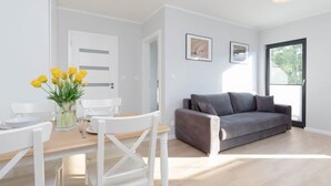 A modern living room with a grey sofa, white chairs, and a dining table with yellow flowers. - Intimate Apartment | SPA & Gym | 550 m to the beach (Miedzywodzie)