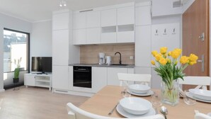 A modern kitchen with white cabinetry, a dining area with a wooden table, and a vase of yellow flowers. - Intimate Apartment | SPA & Gym | 550 m to the beach (Miedzywodzie)