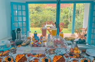 Un buffet de petit-déjeuner proposant une variété d’aliments et de boissons, une machine à café et une vue sur un jardin, accessible par des portes ouvertes.