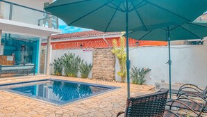 A swimming pool with a tiled deck, a green umbrella, and outdoor seating. - Pousada BellaSophia (Guarujá)