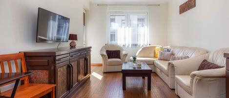 Una sala de estar con televisor de pantalla plana, muebles de madera, un conjunto de sofás y un ventanal con cortinas.