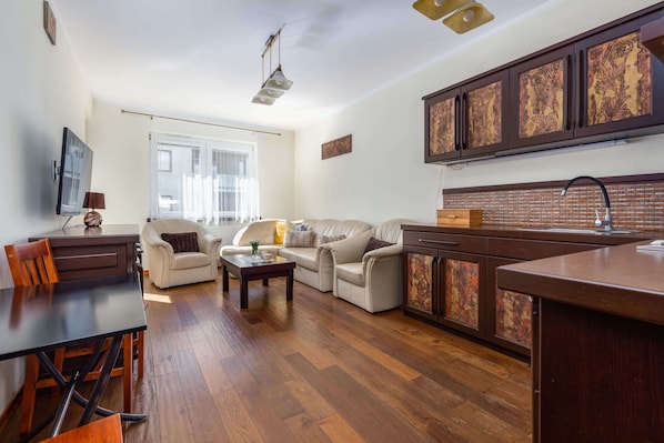A living room with a sofa, a coffee table, a TV, and a dining area with a table and chairs.