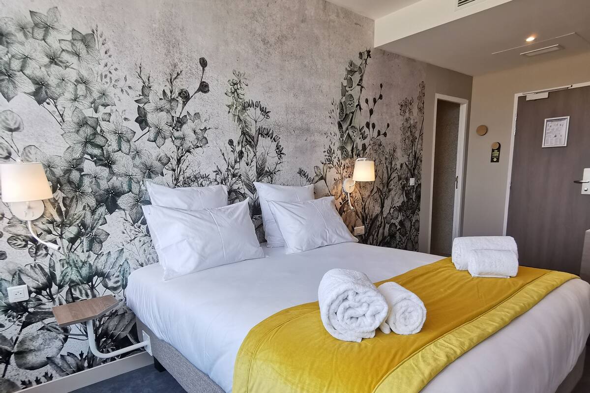 Una habitación de hotel con una cama grande, dos lámparas de noche, un mural floral en la pared y una puerta con un letrero.