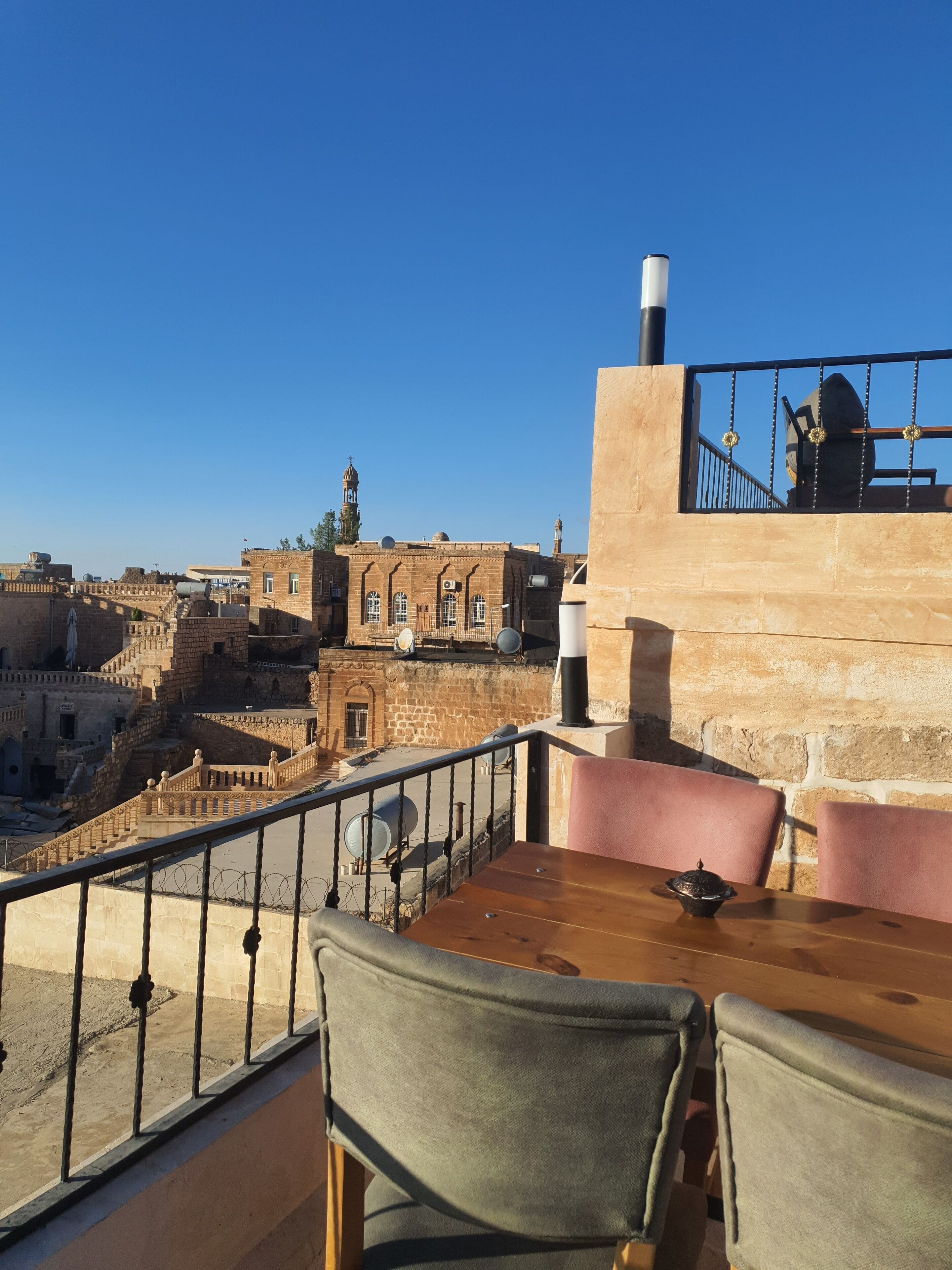 En terrass med utsikt över historiska byggnader, bland annat en moské med ett minaret, och en mur av sten med ett metallräcke.