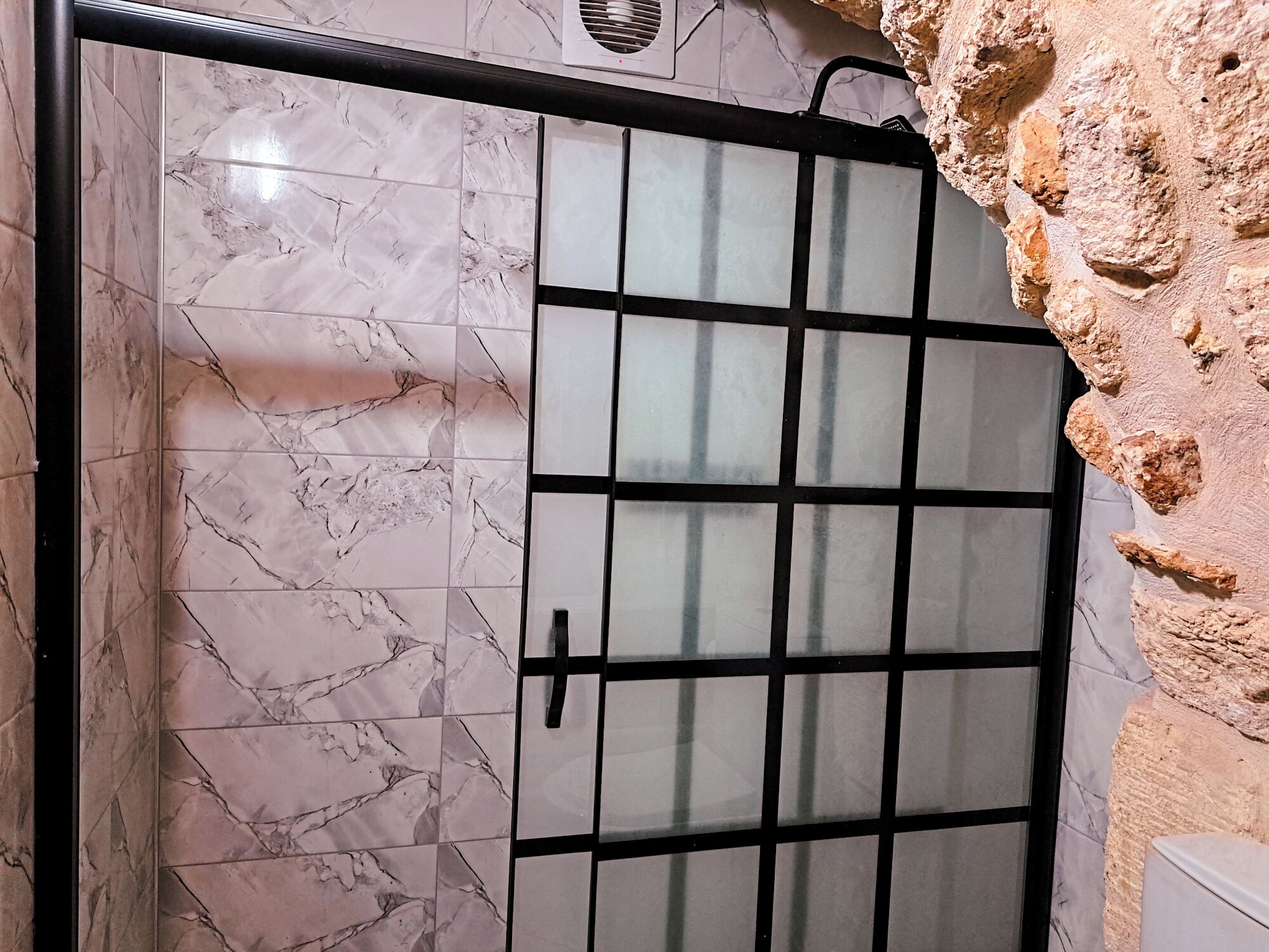 Un baño con baldosas de mármol, cabina de ducha de vidrio y pared de piedra.
