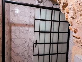 Un baño con baldosas de mármol, cabina de ducha de vidrio y pared de piedra.