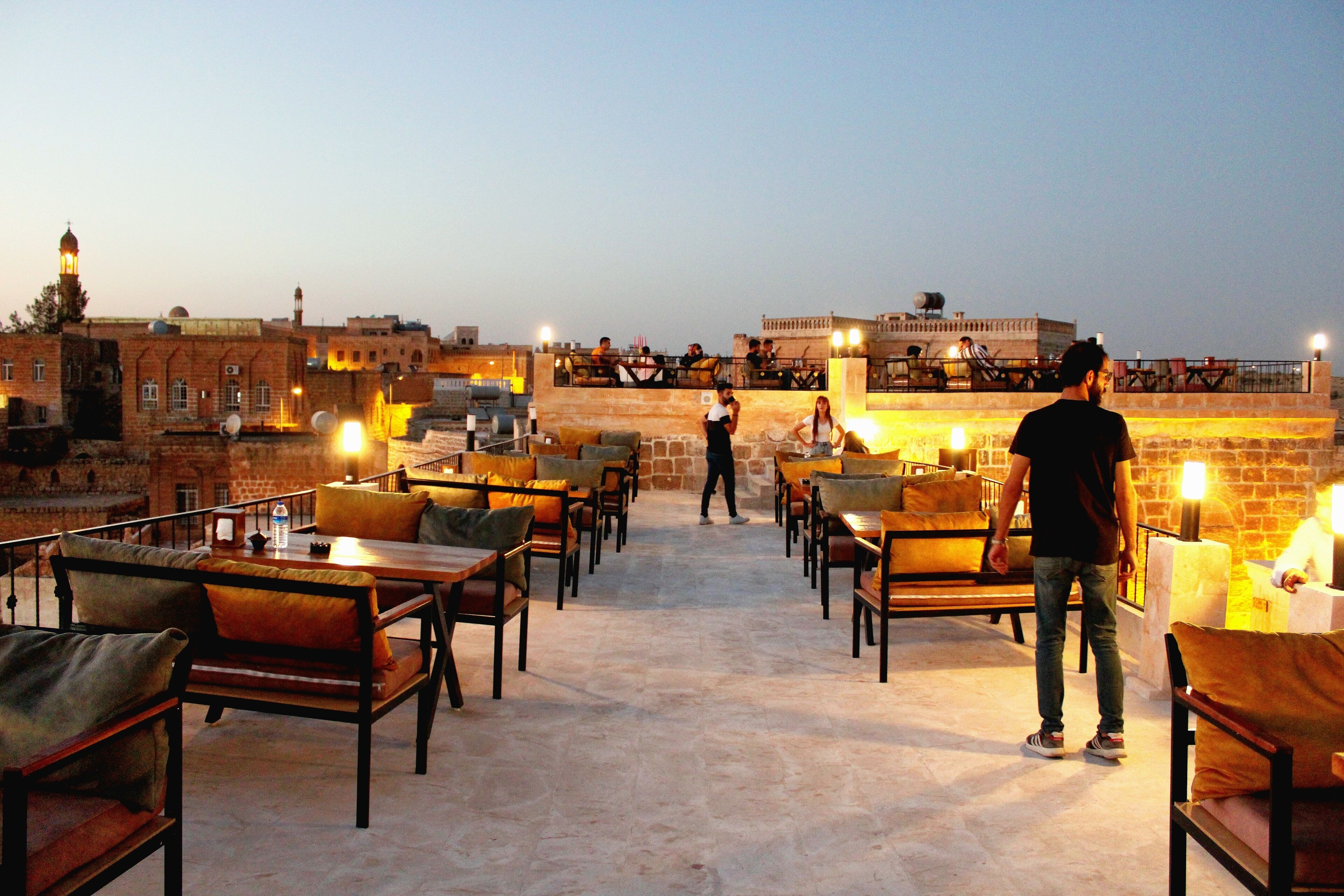 A rooftop terrace with outdoor seating, stone walls, and a view of the cityscape.