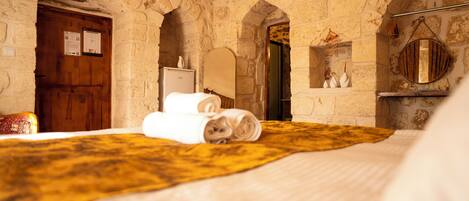 A room with stone walls, a wooden door, a bed with a yellow blanket, and a mirror on the wall.