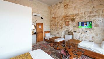 Una habitación con pared de piedra, una cama, una mesa de madera y un televisor.