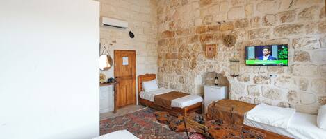 Una habitación con pared de piedra, una cama, una mesa de madera y un televisor.