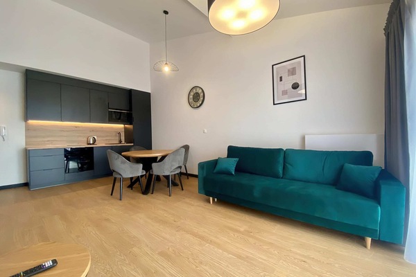 A stylish living area featuring a teal sofa, a round coffee table, and a dining space, blending comfort with modern design.