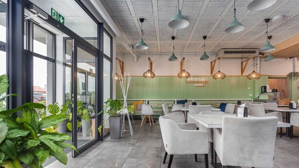 Ein modernes Restaurant-Interieur mit Glastüren, grünen Wänden, weißen Stühlen und Pendelleuchten.
