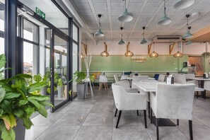 Un interior de restaurante moderno con puertas de cristal, sillas blancas, lámparas colgantes y paredes verdes.