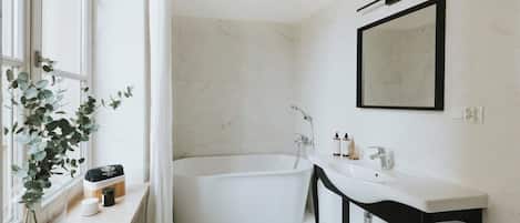 A modern bathroom with a freestanding bathtub, a vanity with a mirror, and a window with a plant.