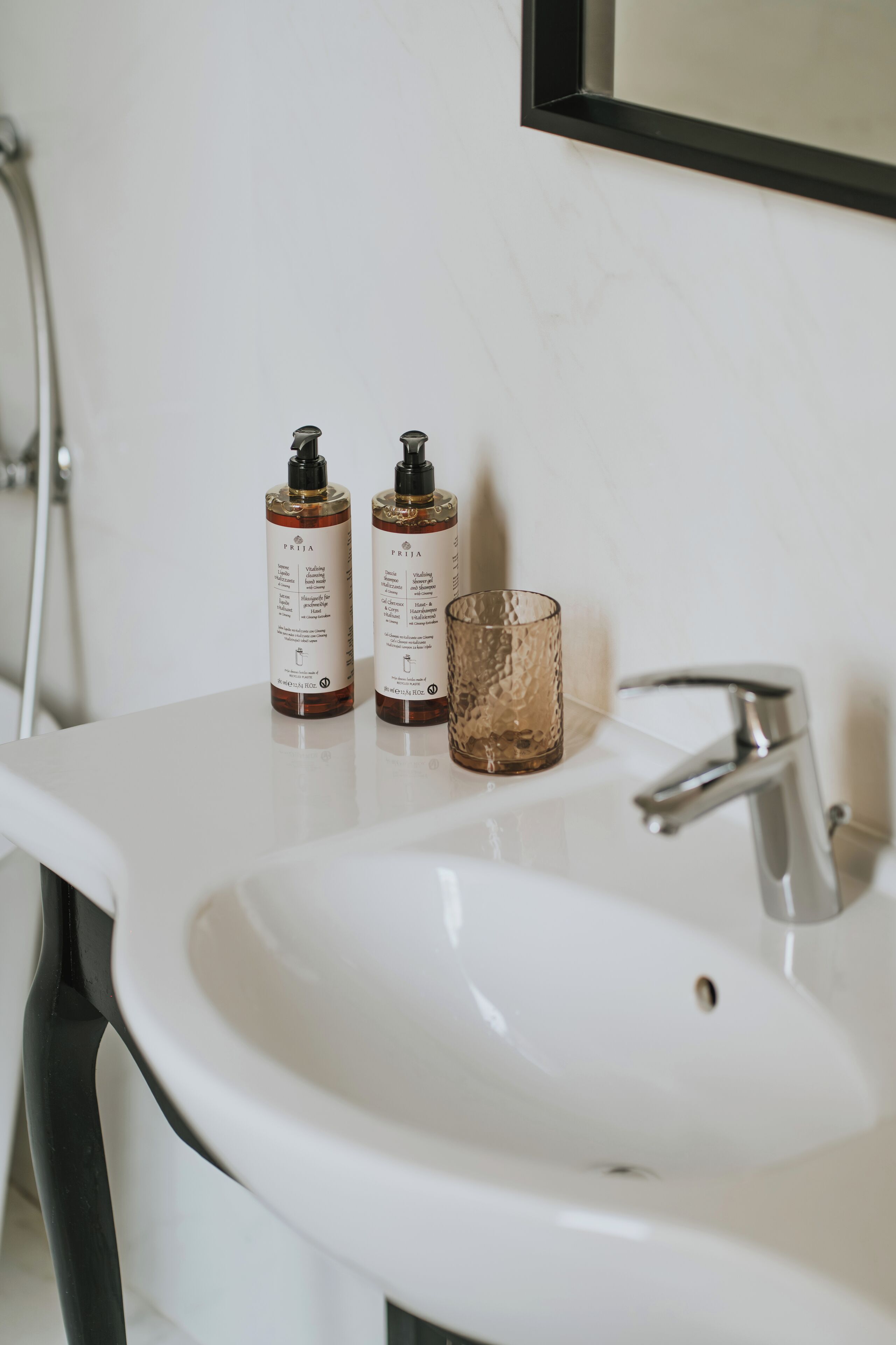 A bathroom sink with two bottles of Frija shampoo and a textured glass.