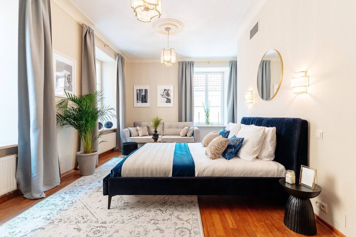 Een slaapkamer met een bed, nachtkastje, lamp en een potplant.