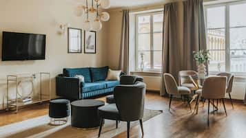A modern living room with a blue sofa, black and white chairs, a round coffee table, and a TV mounted on the wall.