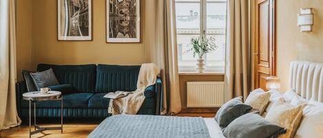 A bedroom with a bed, a dark blue sofa, a small table with a cup, and two framed pictures on the wall.