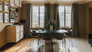 A dining area with a table, chairs, a cabinet, and a large window with curtains. - Bogoria House (Kraków)