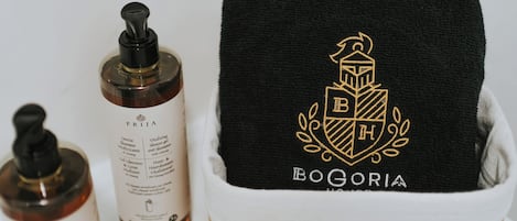A bathroom with a wooden tub, a black towel with a crest, and two bottles of shampoo.