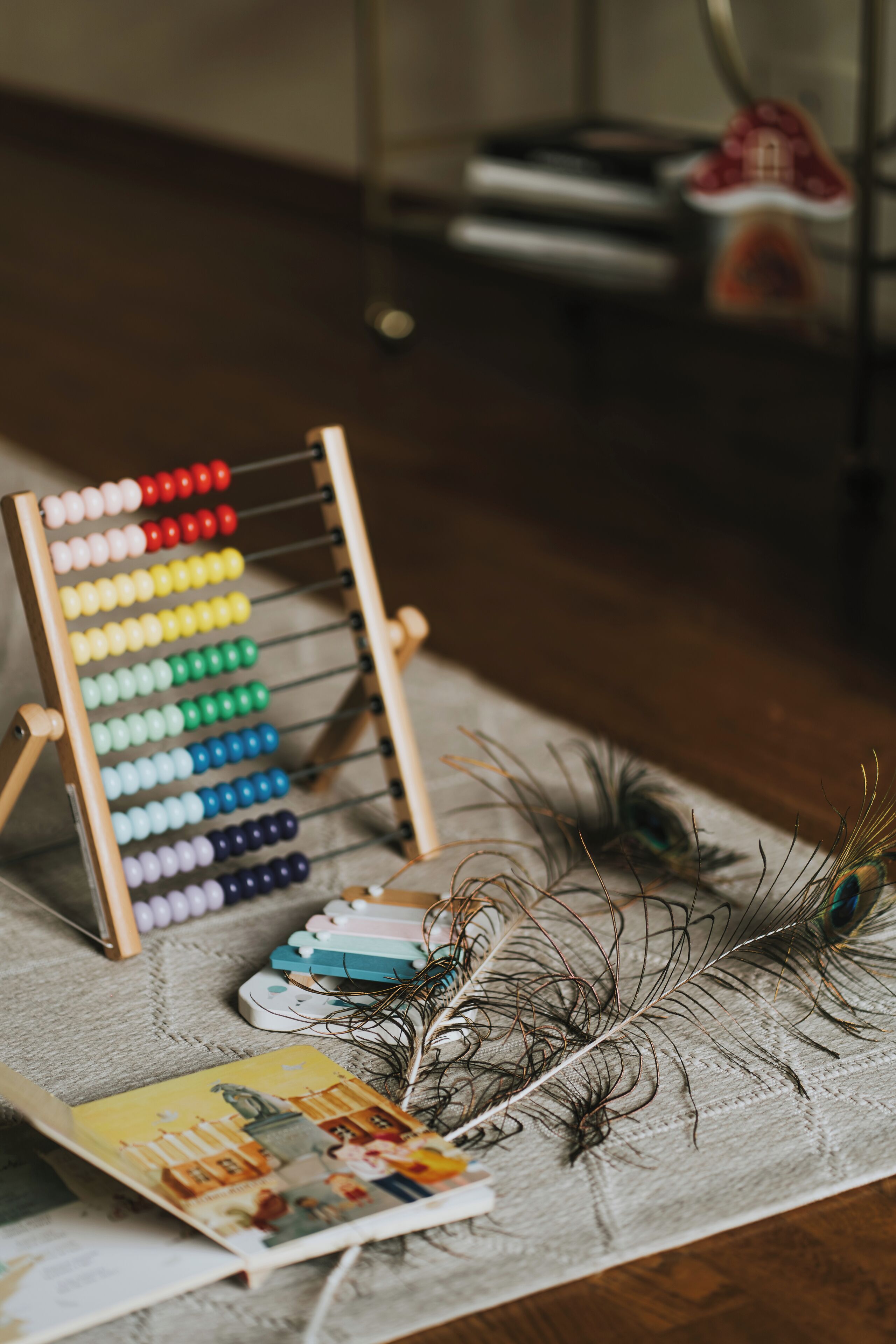 A wooden abacus with colorful beads, a feather, and a book on a textured surface.